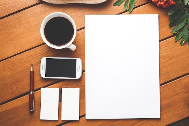 Blank piece of paper, cup of coffee, phone, and pen all sitting on a table, image used for Ryan Stoner blog on the importance of creating a brand story for your business